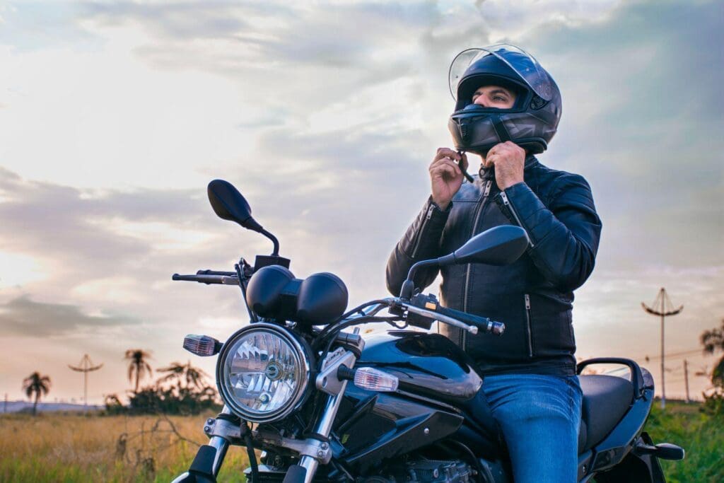 Man adjust his motorcycle helmet while sitting on his bike