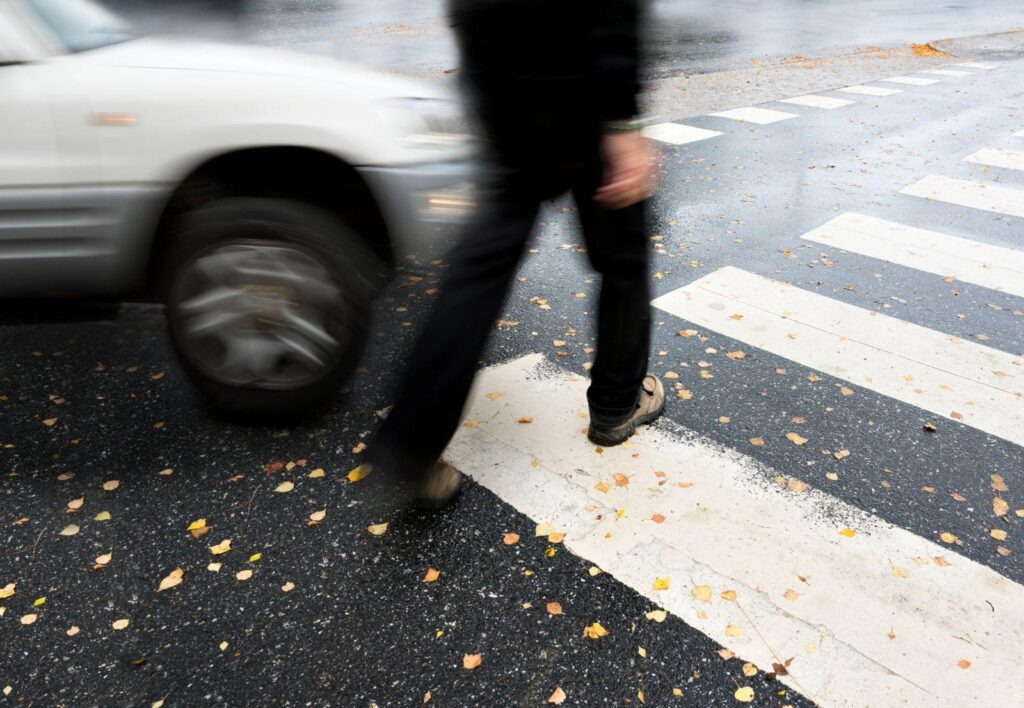 A blurry picture of a man walking in front of a car in a crosswalk.