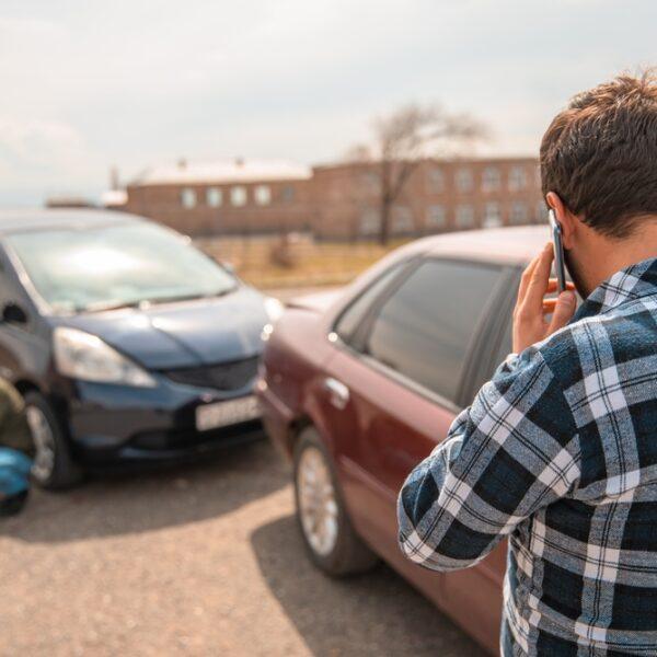 Man on his phone standing in front of two vehicles involved in an auto collision and wondering what to do after a car accident.