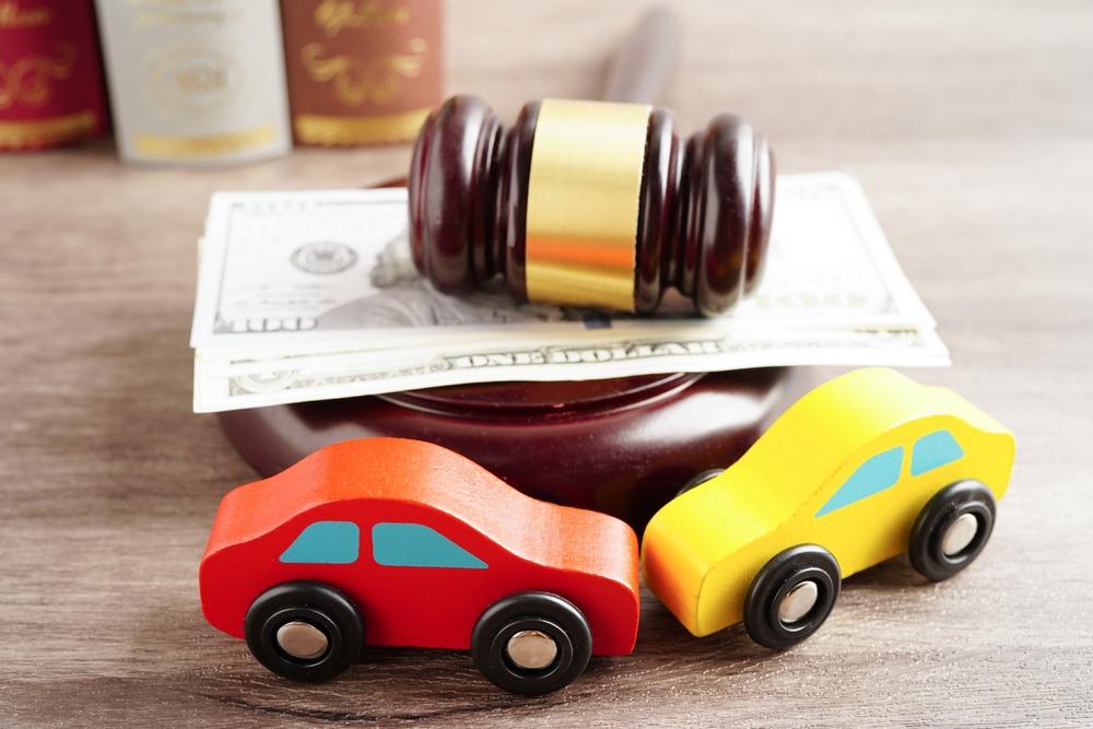 Toy cars on a desk near a gavel and money to signify a legal case that asks the question, “How much money can a passenger get after a car accident?”