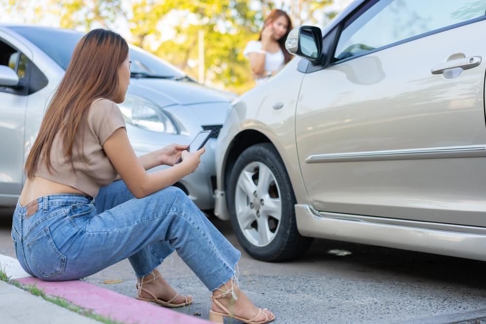 Two women sit outside of a car accident. Will my insurance cover an accident in someone else’s car?