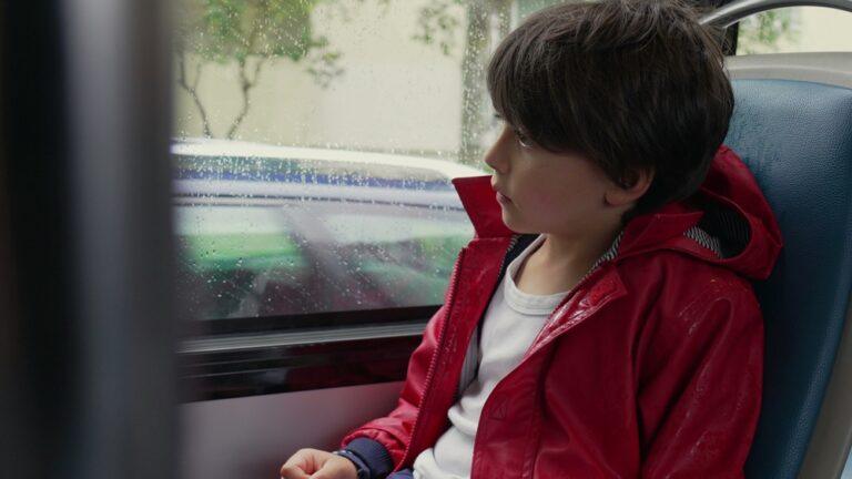 A child with brown hair and a red jacket sits in a school bus showing the most common signs of child sexual abuse. 