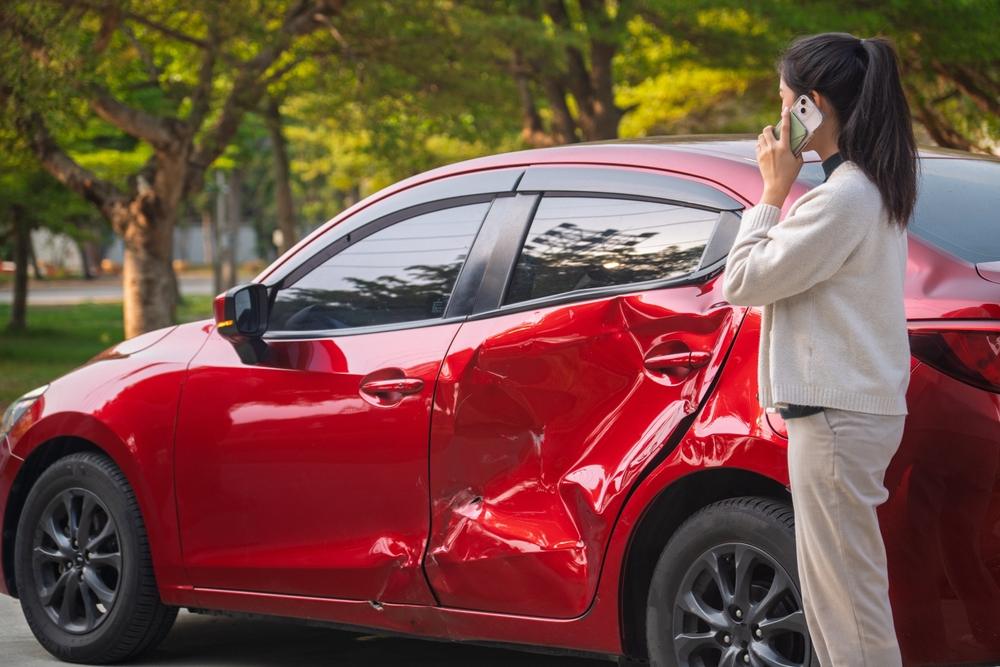 Woman stands next to a damaged car and calls her lawyer after a rubbernecking accident.