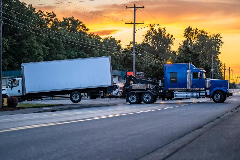 A white commercial truck being towed by another truck as they wonder how much a truck accident lawyer costs