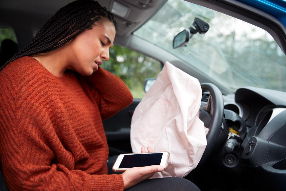 Woman in the driver's seat of a car with a deployed airbag after a crash is using her phone to ask about what to do if an Amazon truck hits your car.