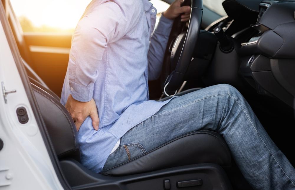 A man sitting in a car and clutching his back. Learn about how much a bulging disc injury is worth in a car accident.