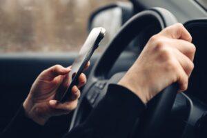 A person texting while driving who needs to learn the definition of distracted driving.