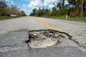 Damaged road surface with deep pothole. What are the most dangerous highways in America?